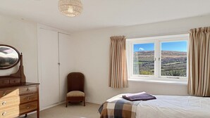 A bedroom with two beds, a dresser, a chair, a window with curtains, and a hanging light fixture. - Brightworthy Farm, Withypool on Exmoor (Withypool)