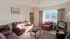 A living room with a brown leather sofa, a pink armchair, a wooden coffee table, and a television on a stand. - Brightworthy Farm, Withypool on Exmoor (Withypool)