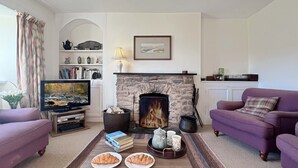 A living room with a fireplace, two purple sofas, a coffee table with croissants, a television, and a bookshelf. - Brightworthy Farm, Withypool on Exmoor (Withypool)