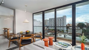 A modern living room with a dining area, large windows, and a view of the cityscape.