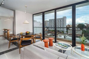 A modern living room with a dining area, large windows, and a view of the cityscape.