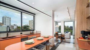 A modern kitchen with a large window, a dining area with a table and chairs, and a view of the cityscape.