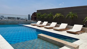 Una piscina en la azotea con sillones de descanso y palmeras.