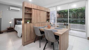 Un espacio habitable moderno y funcional con kitchenette, comedor y balcón con vistas a zonas verdes.