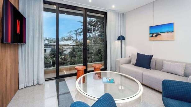 A modern living room with a sofa, a glass coffee table, and a TV mounted on the wall. - Deluxe 2-Bed • By Cali's Best Restaurants | 301 (Cali)