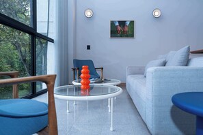 Un saló modern amb un sofà, dues cadires, una taula de café de vidre i un objecte vermell, i un quadre a la paret.