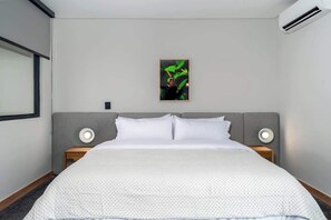 Una habitació d'hotel amb un llit gran, dues làmpades de nit, aire condicionat fixat a la paret i un quadre encimbellat.