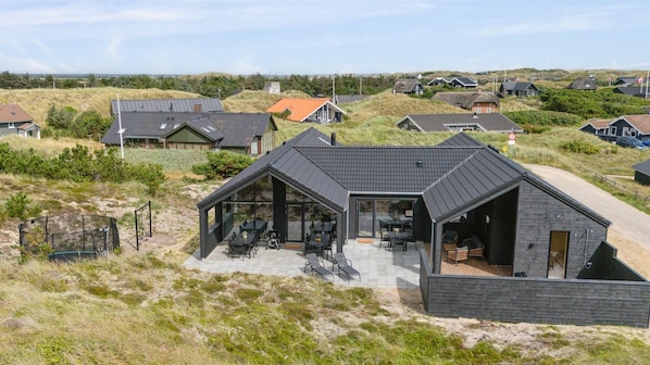 A modern house with a large glass patio area, surrounded by a dune landscape.