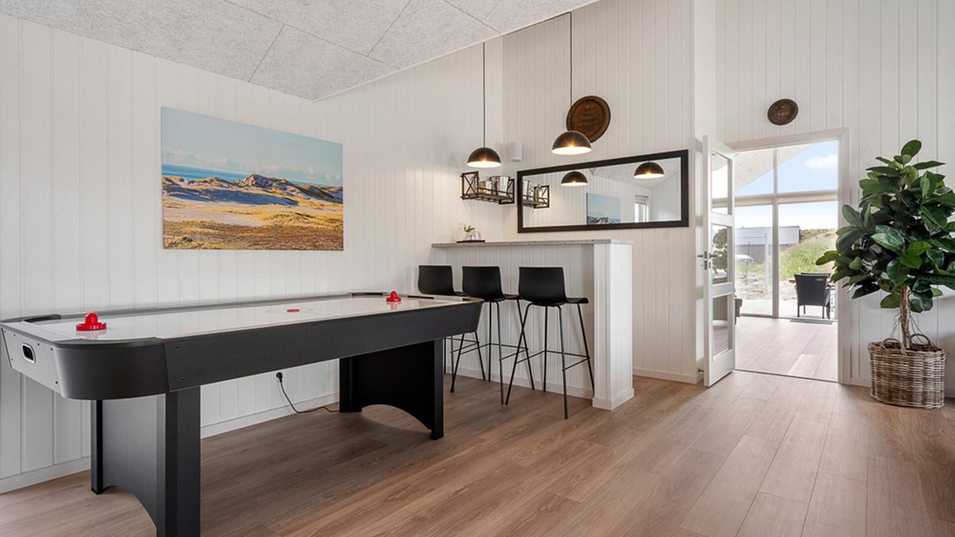 Une table de billard avec des chaises, un coin bar, un grand miroir et une vue à travers une porte.