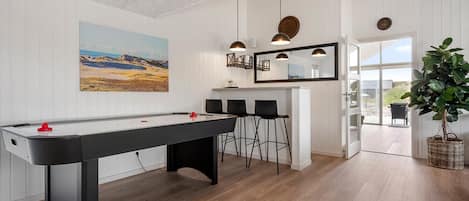 A pool table with chairs, a bar area, a large mirror, and a view through a door.