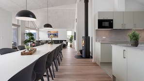 A modern kitchen with a central island, black pendant lights, and a microwave above the cabinets. - VillaVilla 943 - Hvide Sande, Vestjylland (Hvide Sande)