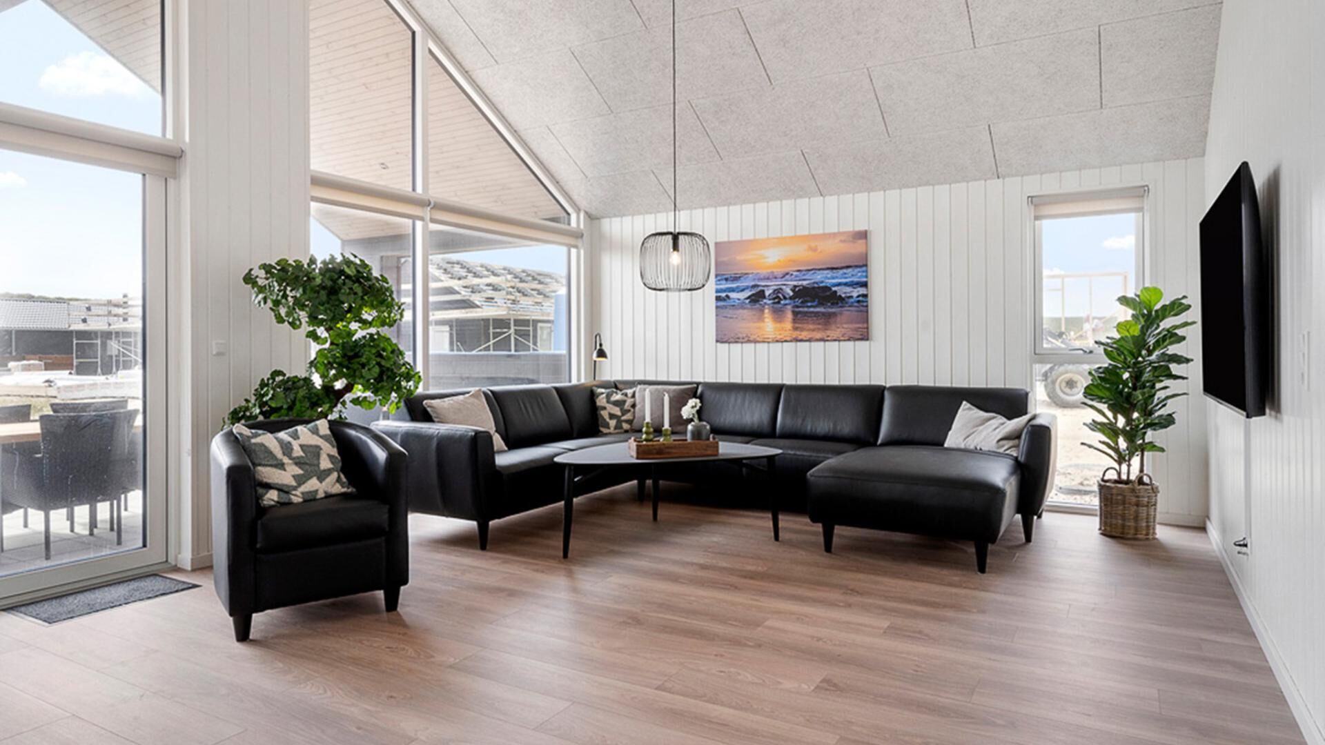 Un salon moderne avec un canapé d’angle, une table basse et une grande fenêtre donnant sur l’extérieur.