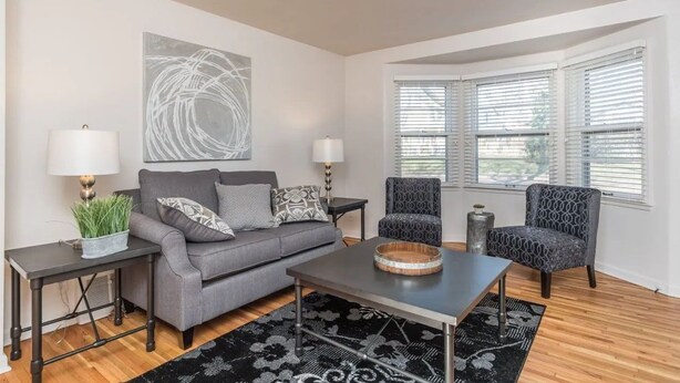 A living room with a gray sofa, two patterned armchairs, a coffee table, a side table with a lamp, and a large abstract painting on the wall. - Perfect 2-bedroom apartment near McKennan Park and Downtown! (Sioux Falls)