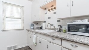 A modern kitchen with white cabinets, a granite countertop, a built-in microwave, and a window with blinds. - Perfect 2-bedroom apartment near McKennan Park and Downtown! (Sioux Falls)