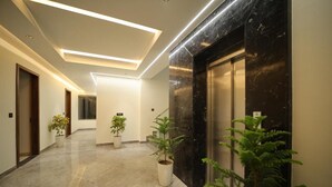 A modern hallway with marble flooring, potted plants, and a black elevator. - Hotel RS (Agra)