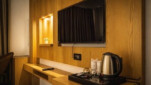 A hotel room with a wooden desk, a television mounted on the wall, a coffee maker, and a tray with a glass and a bottle. - Hotel RS (Agra)