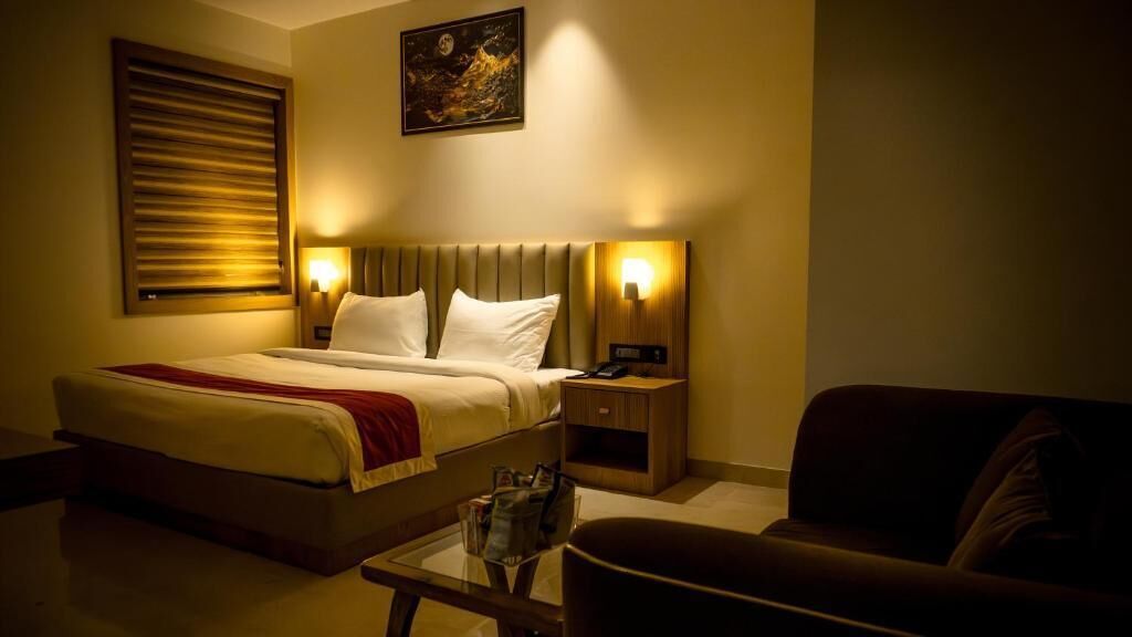 A hotel room with a bed, bedside tables, a nightstand, a sofa, and a wall-mounted artwork.