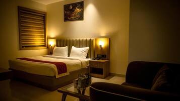 A hotel room with a bed, bedside tables, a nightstand, a sofa, and a wall-mounted artwork.