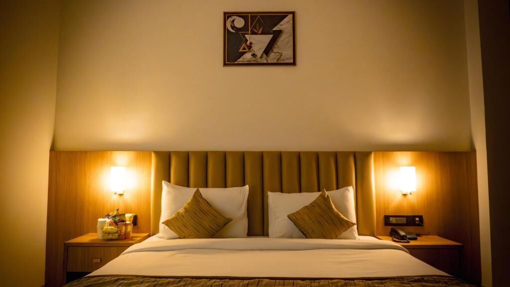 A hotel room with a large bed, two bedside tables, a wall-mounted artwork, and two wall-mounted lamps.