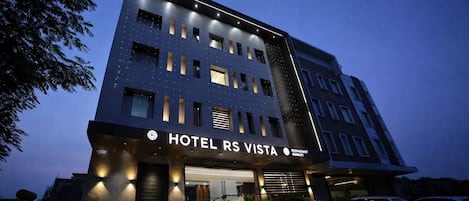 A multi-story hotel with a modern design, featuring a prominent entrance, a restaurant, and a parking area.