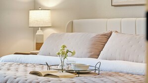 A neatly made bed with a white duvet, a bedside table with a lamp, and a tray with a vase of flowers, a glass, and a bowl. - Walk in NO STAIRS 2 Bedroom Condo in Pointe Royale Golf Village NEW FOR 2026 (Branson)
