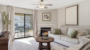 A modern living room with a fireplace, a ceiling fan, and a large window overlooking a patio. - Walk in NO STAIRS 2 Bedroom Condo in Pointe Royale Golf Village NEW FOR 2026 (Branson)