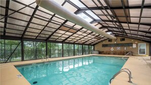 An indoor swimming pool with a metal roof and glass walls, surrounded by a fence. - Walk in NO STAIRS 2 Bedroom Condo in Pointe Royale Golf Village NEW FOR 2026 (Branson)