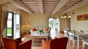 A spacious living area with a high wooden ceiling, a sofa set, a dining table, and a view through an open door to a garden. - 2 bedroom awesome apartment in Trequanda (Trequanda)