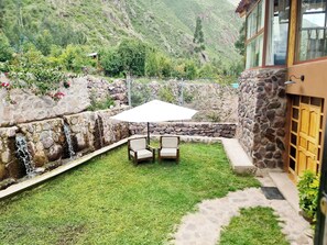 A stone-walled outdoor seating area with a table and chairs, a white umbrella, and a view of a mountainous landscape. - Beautiful home overlooking Arin Waterfall and Mountains, crystal clear creek (Calca)