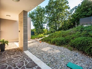 Ein moderner Außenbereich mit einem Steinweg, einer grünen Matte und einem Garten mit verschiedenen Pflanzen und Bäumen.