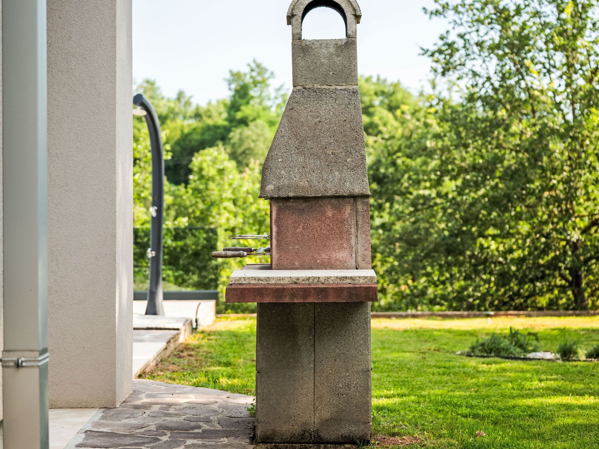 Ein Stein-Barbecue-Grill mit Metallgriff in einer grünen Außenanlage.