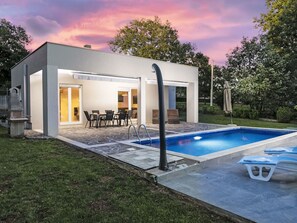Ein moderner Poolbereich im Freien mit überdachter Lounge und klarem Wasser.