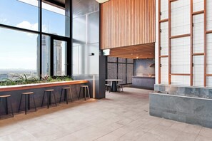 Un espace bar moderne, doté de hauts plafonds, de grandes fenêtres et offrant une vue sur le paysage urbain.
