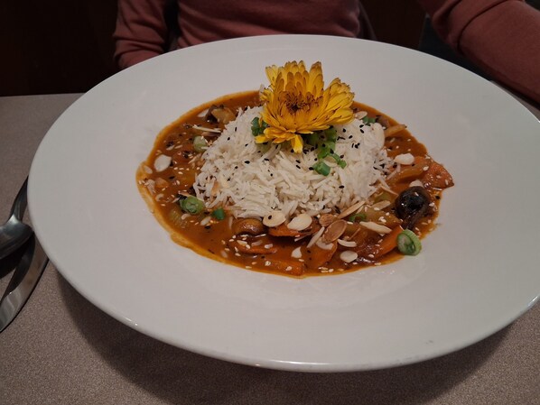 A white plate with a dish of rice, vegetables, and a flower garnish. - The Orca Inn (Alert Bay)