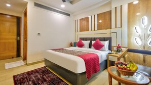 Une chambre d’hôtel avec un lit, une table de chevet sur laquelle se trouve un panier de fruits, un miroir avec éclairage et un ventilateur de plafond.