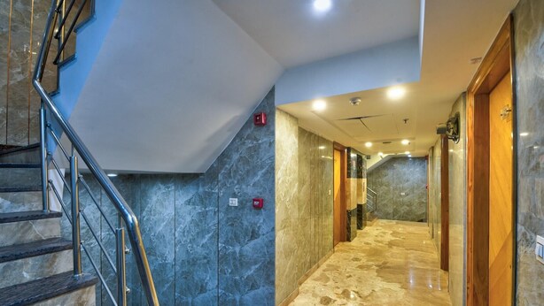 Un couloir d’hôtel aux murs de marbre, un escalier avec des rampes en métal et une porte en bois sur la droite.