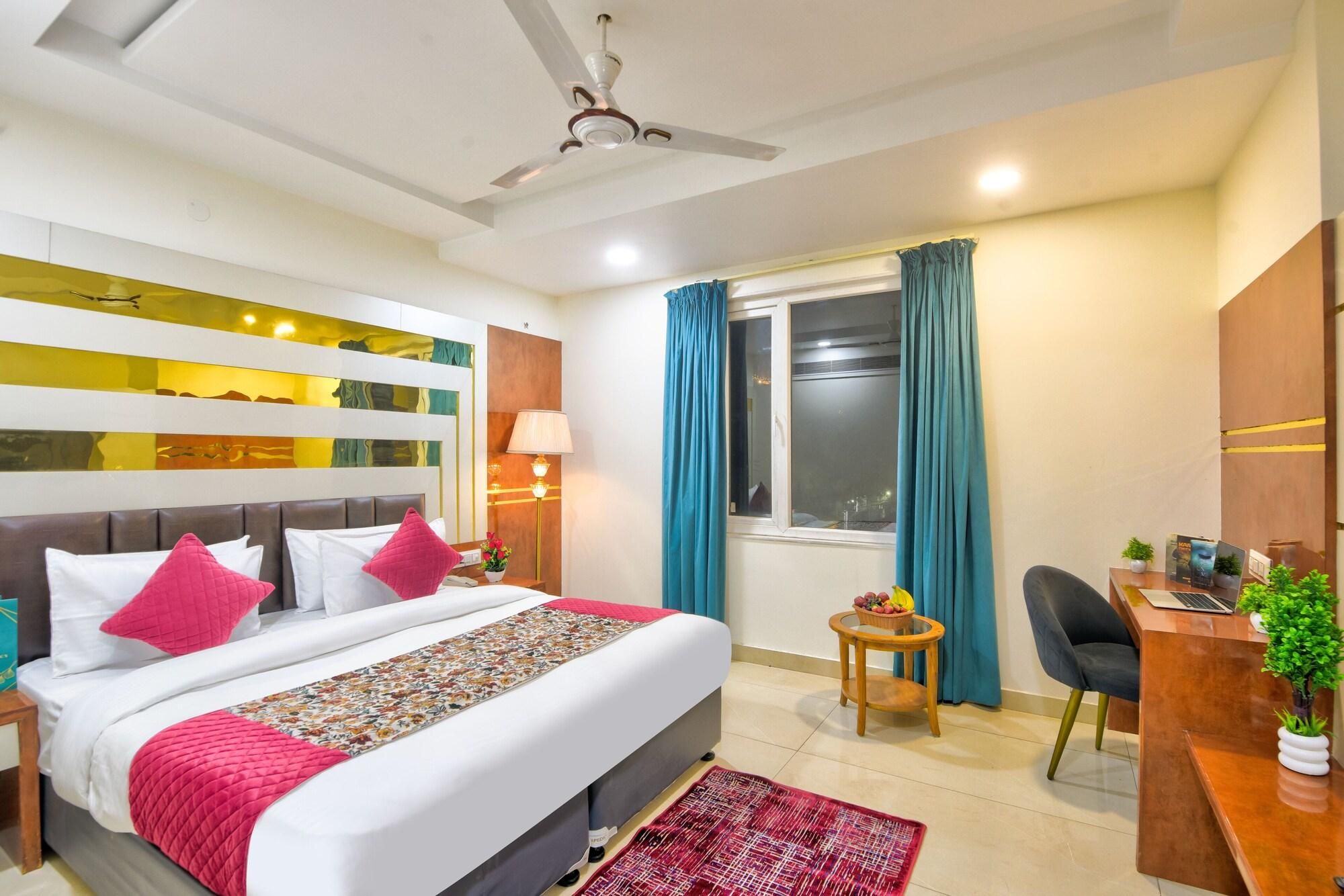 Una habitación de hotel con una cama, un escritorio, una silla, una ventana con cortinas, un ventilador de techo y un panel decorativo en la pared.