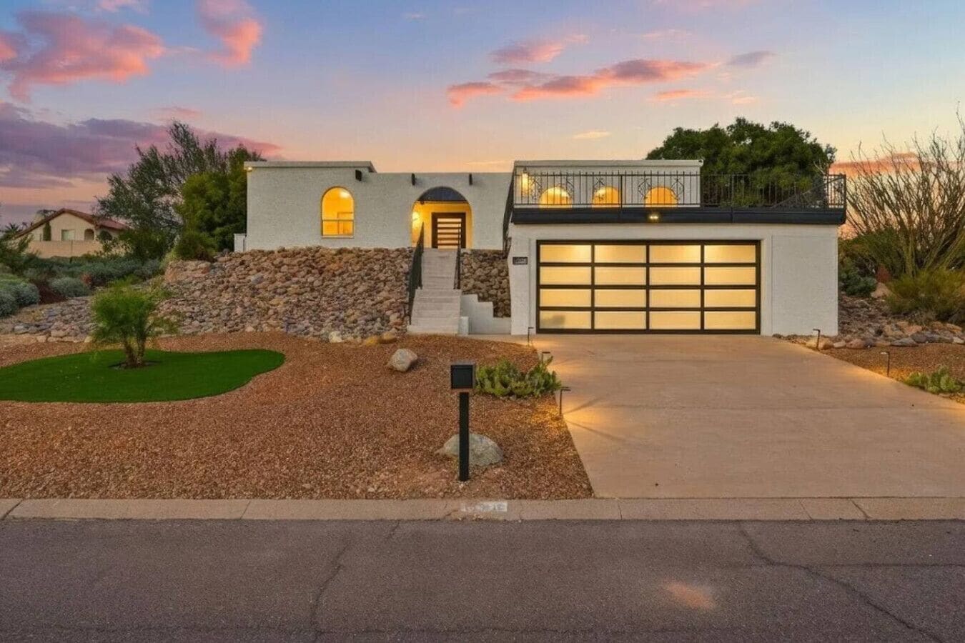 Une maison moderne à deux étages, dotée d’un garage, d’un mur de soutènement en pierre et d’un jardin paysager à l’avant.