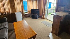 Un salon avec un canapé, une table en bois, un téléviseur et un balcon agrémenté de rideaux.