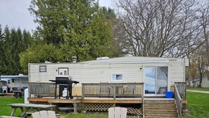 Une maison mobile dotée d’une terrasse, de deux fauteuils Adirondack et d’un foyer extérieur.