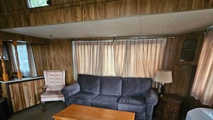 Un salon avec un mur lambrissé en bois, un canapé gris, une table basse en bois, un fauteuil blanc et une lampe.