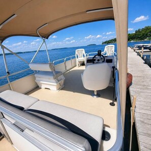 A boat deck with seating, a steering wheel, and a view of the water.