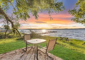 A table and chairs set on a grassy area with a view of a body of water and a dock in the background. - #8 Cottage - Chile Lakefront (Hamilton)