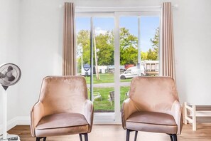 A room with two leather chairs, a standing fan, and a sliding glass door leading to an outdoor area with greenery and parked vehicles. - #6 Cottage - Mexico (Hamilton)