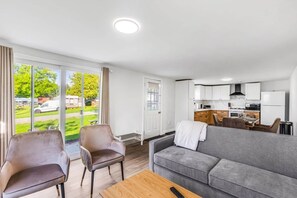 A modern living room with a grey sofa, two armchairs, a wooden coffee table, and a view of the outside. - #6 Cottage - Mexico (Hamilton)