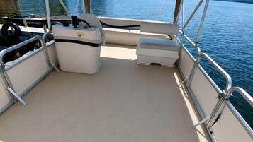 A boat's deck with a covered seating area, a steering wheel, and a small cooler.