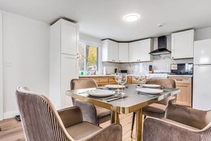 A modern kitchen with white cabinets, a gas stove, and a dining area with a table set for four. - #6 Cottage - Mexico (Hamilton)