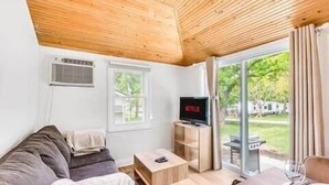 A room with a wooden ceiling, a sofa, a TV, a table, and a sliding glass door leading to an outdoor area.