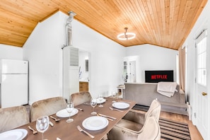 Un comedor con techo de madera, paredes blancas y un televisor con la etiqueta 'NETFLIX' al fondo.