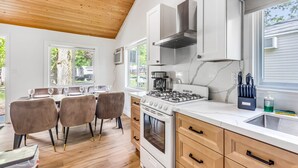 A modern kitchen with a gas stove, oven, and white cabinets. There is a dining area with a table and chairs.